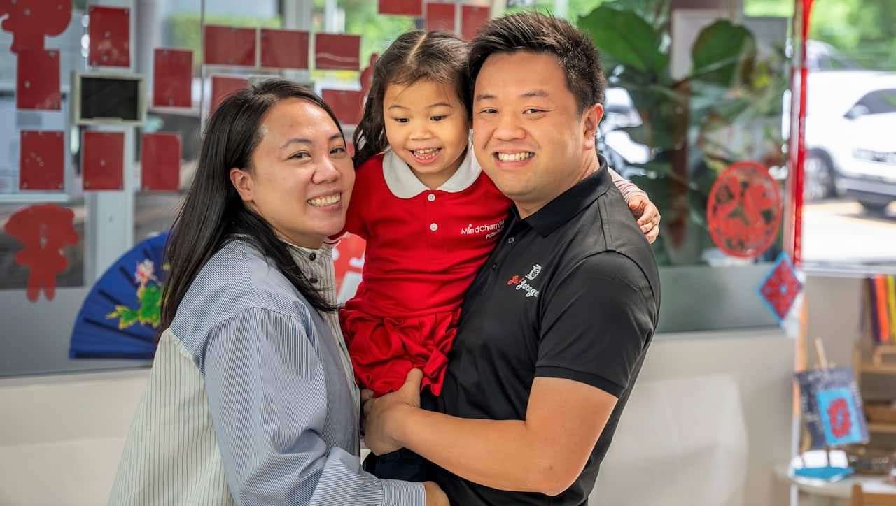 A woman in a striped shirt holds a young child in a red dress with a man in a black t-shirt.