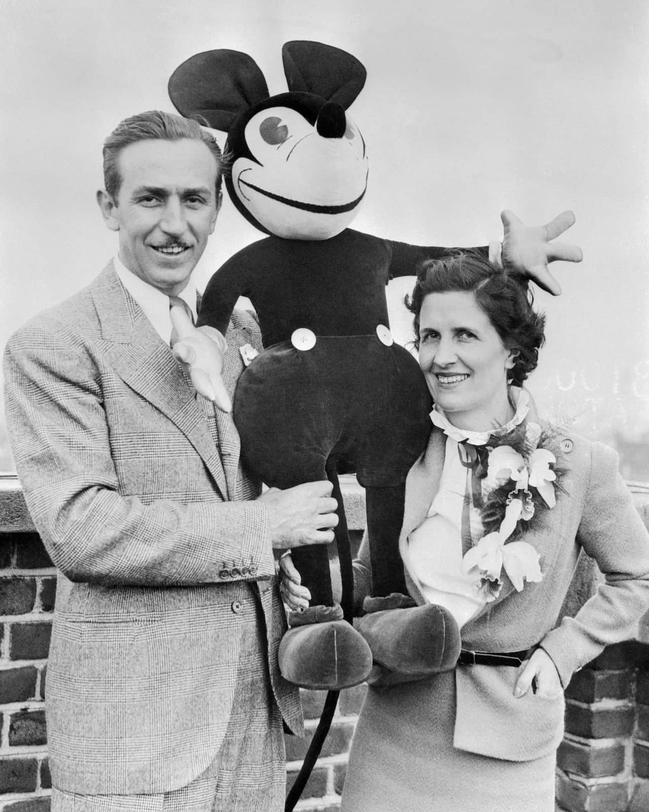 A man and woman standing next to each other. The man is holding up a large plush Mickey Mouse.