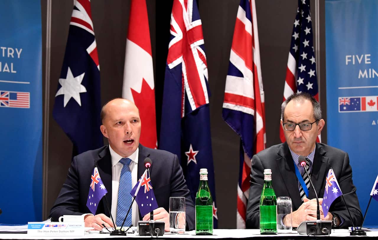 Peter Dutton and Mike Pezzullo standing at a desk behind five countries' flags.