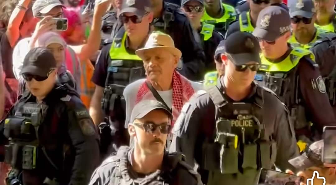 A man wearing a keffiyeh being arrested by police