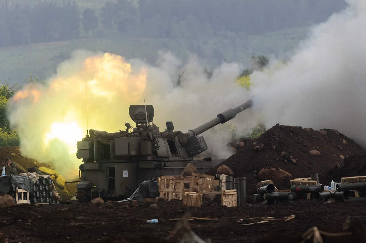 Plumes of smoke surround a military tank with wooden boxes, artillery and mounds of mud in the foreground.
