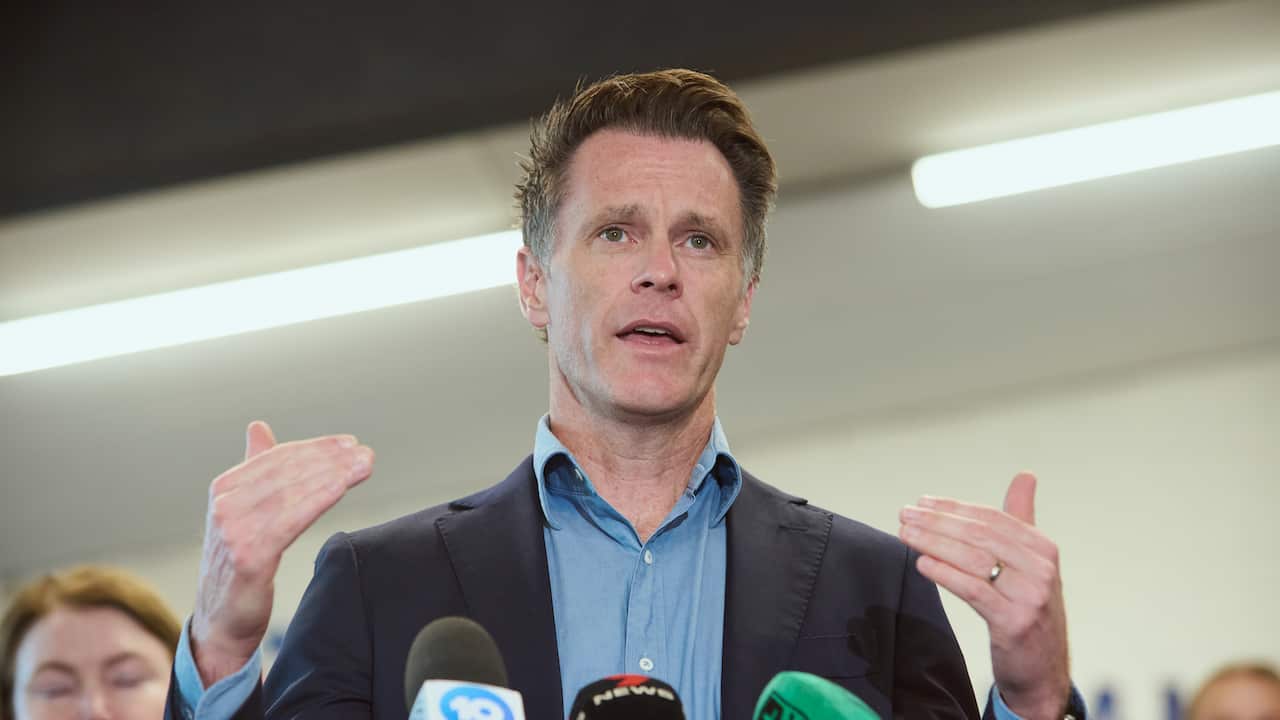 A man in a blue suit speaks into press microphones while gesturing.