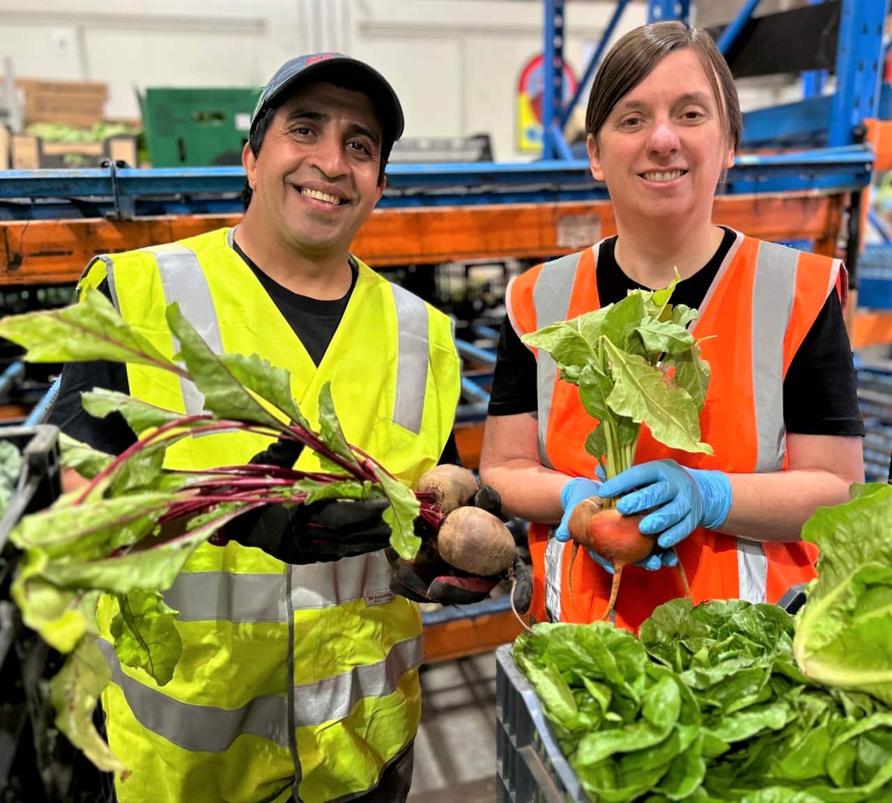 A man in a hi-viz vest holding vegetables standing next to a woman also wearing   a hi-viz vest.