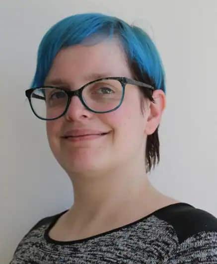 A woman with blue hair and glasses smiling