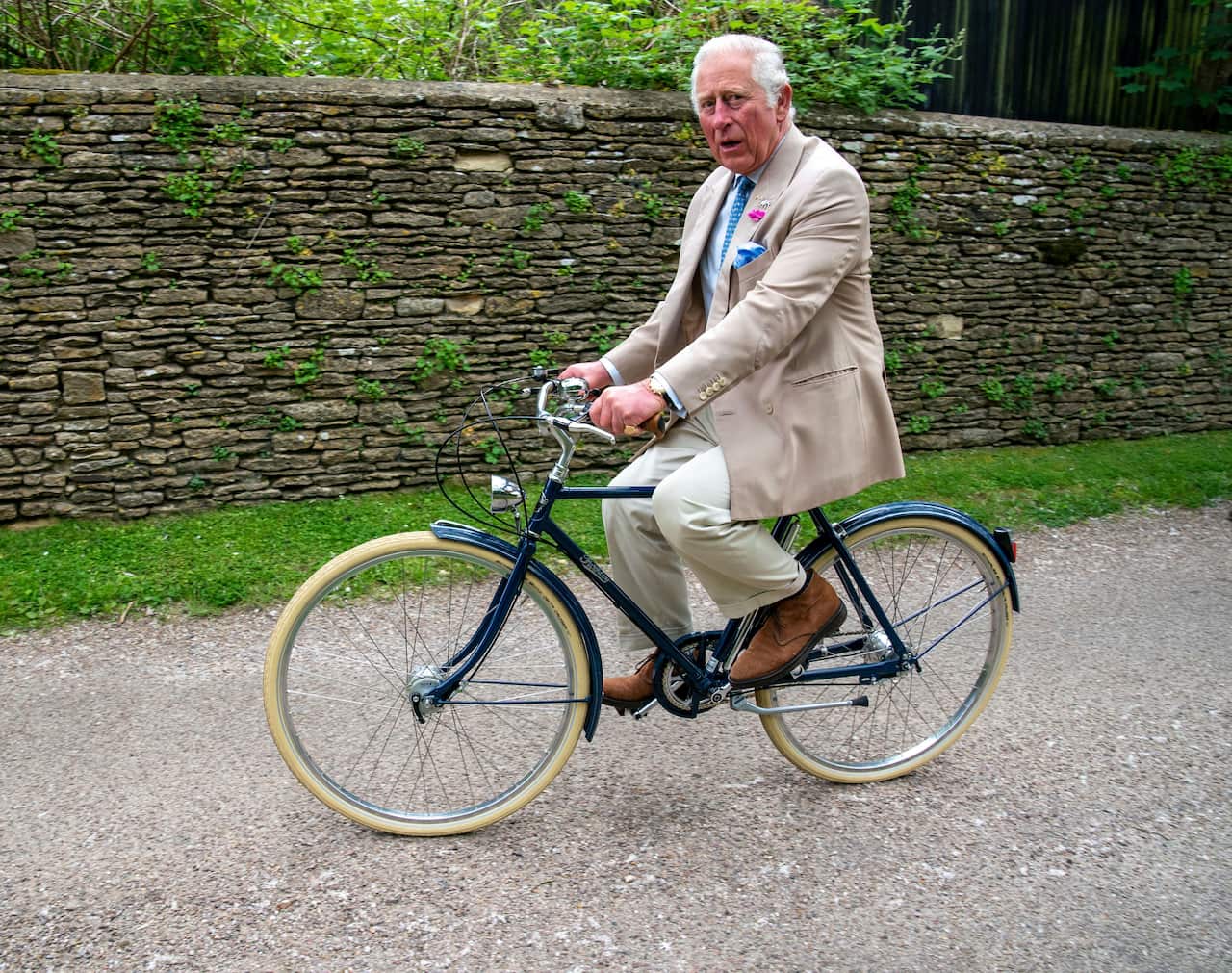 Then-Prince Charles riding a bicycle while wearing a suit.