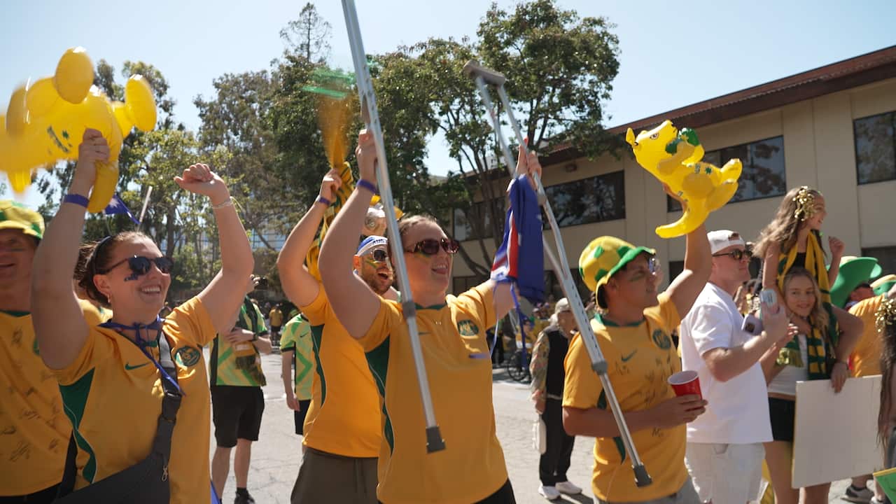 Australian football fans in green and gold marching down a street. A woman is holding crutches in the air.