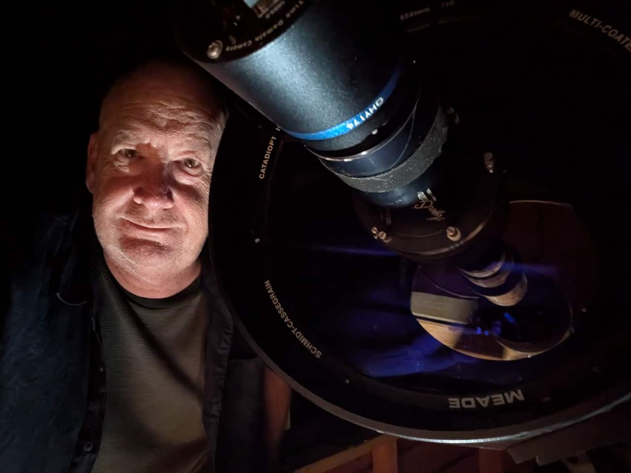 A close-up image of a man standing with his telescope in the night.