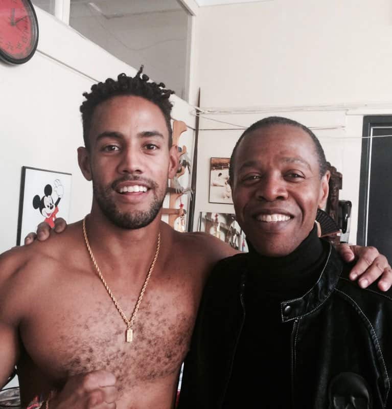 A bare chested man with his arm around an older man 