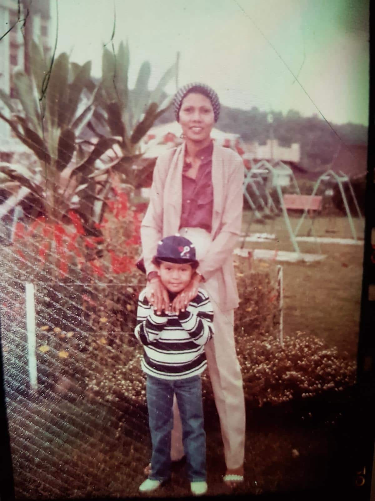 A small child with a black and white striped shirt stands in front of her mother, with the mothers hands on her shoulders. 