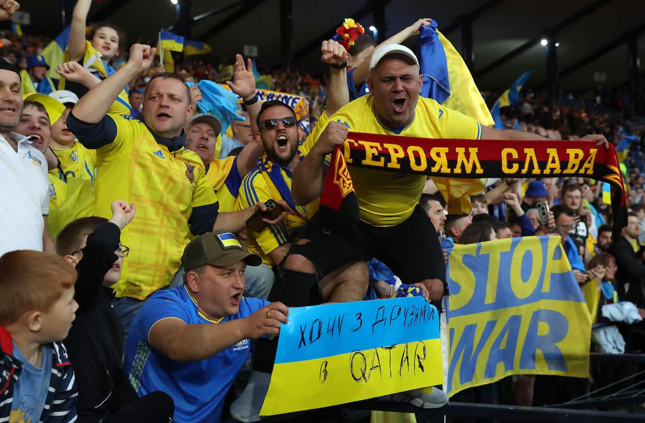 A group of people cheering and holding scarves and signs, one that reads "stop war".