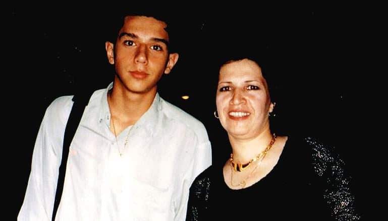 A young man (left) and his mother stand together looking at the camera