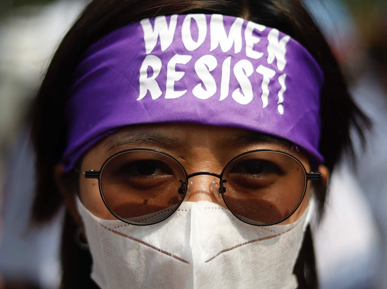 Close up of a woman wearing a purple bandana that says 'women resist'.