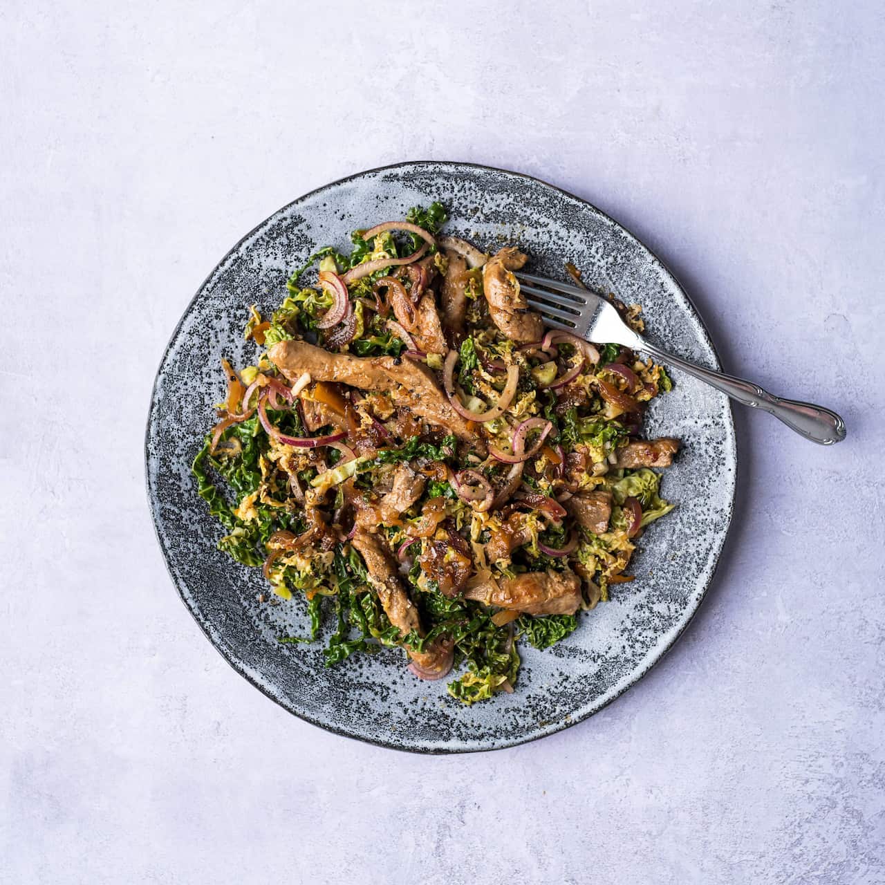 A plate of cooked pork and greens sits on a blue-grey plate. 