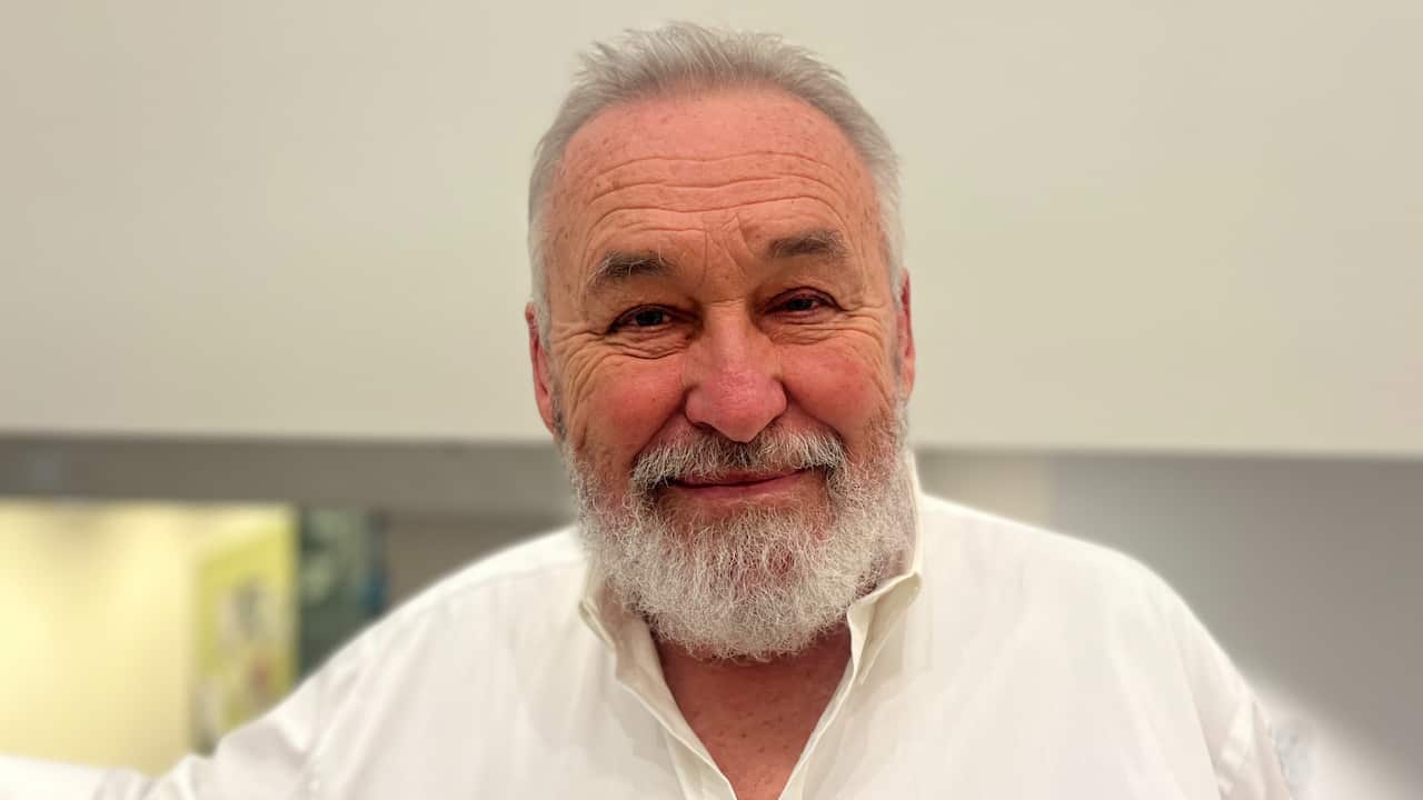 a close up of an older man with grey hair and a grey beard wearing a white shirt