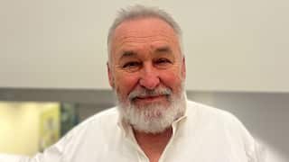 a close up of an older man with grey hair and a grey beard wearing a white shirt