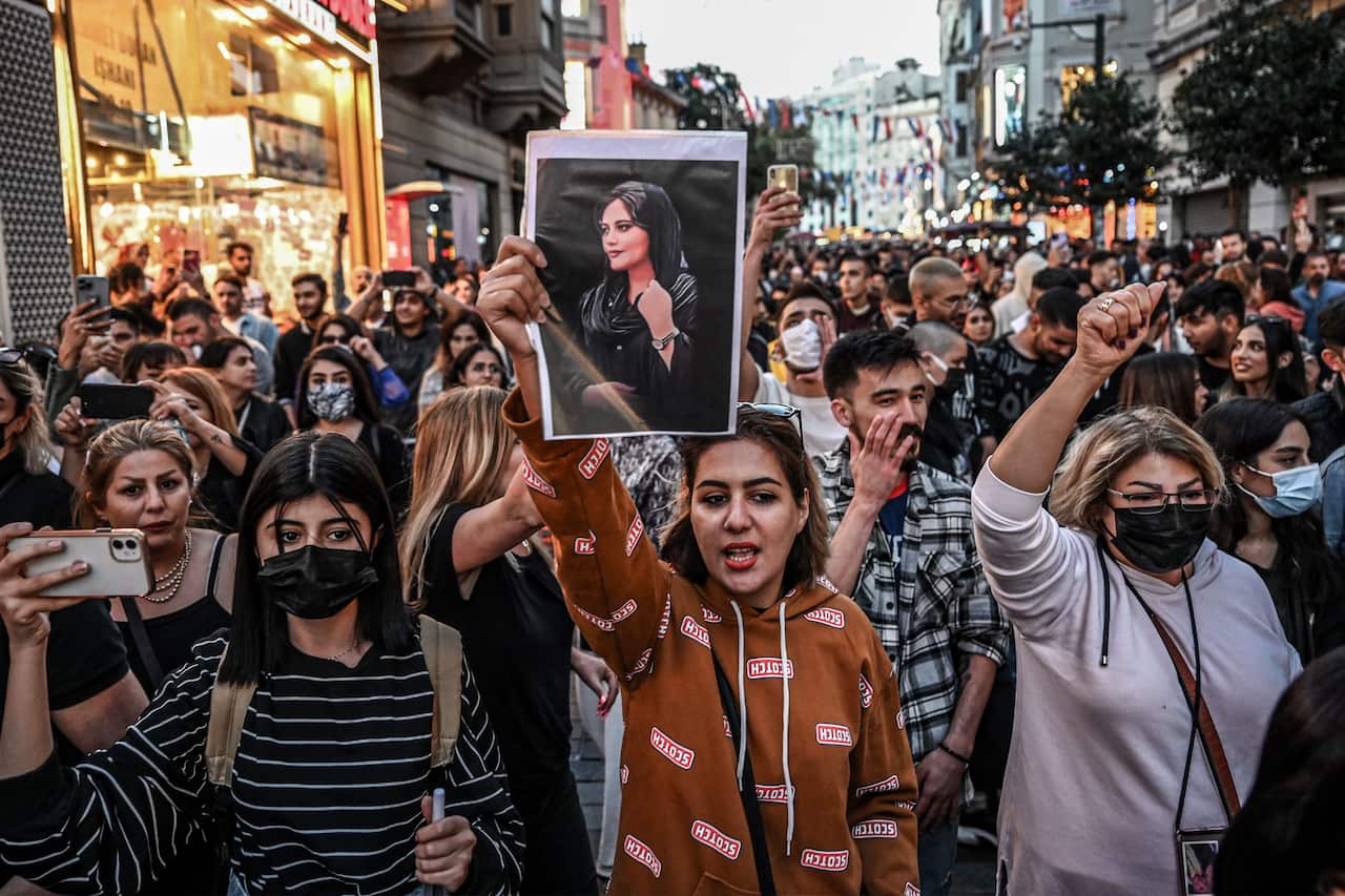 A crowd of demonstrators march down a street. One is holding a photo of a woman.