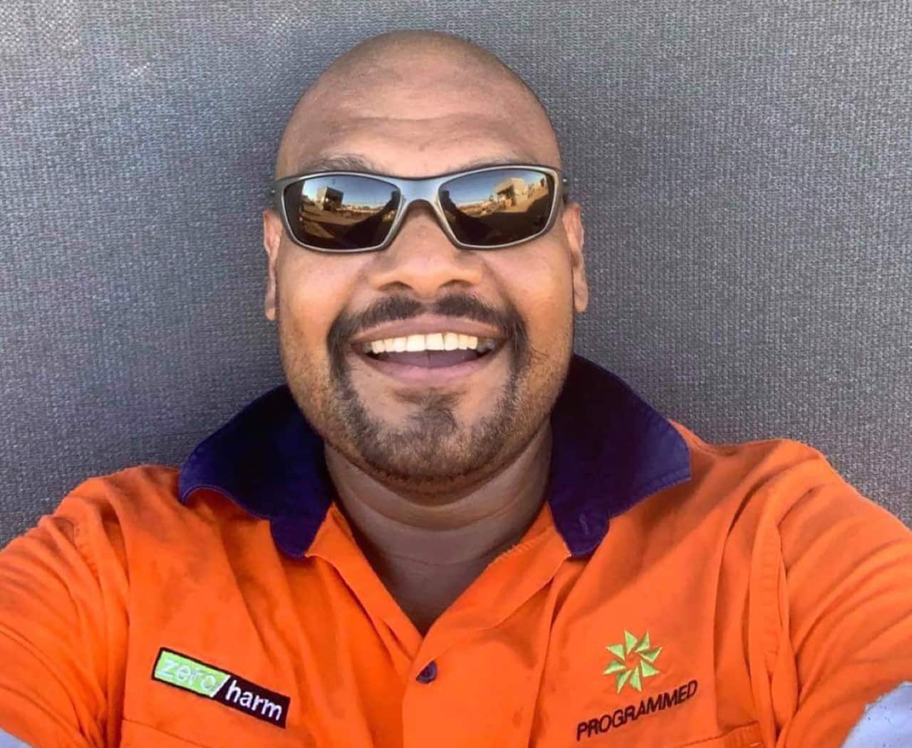 A Noongar man in a hi-vis mining uniform and sunglasses beams into the camera for a selfie