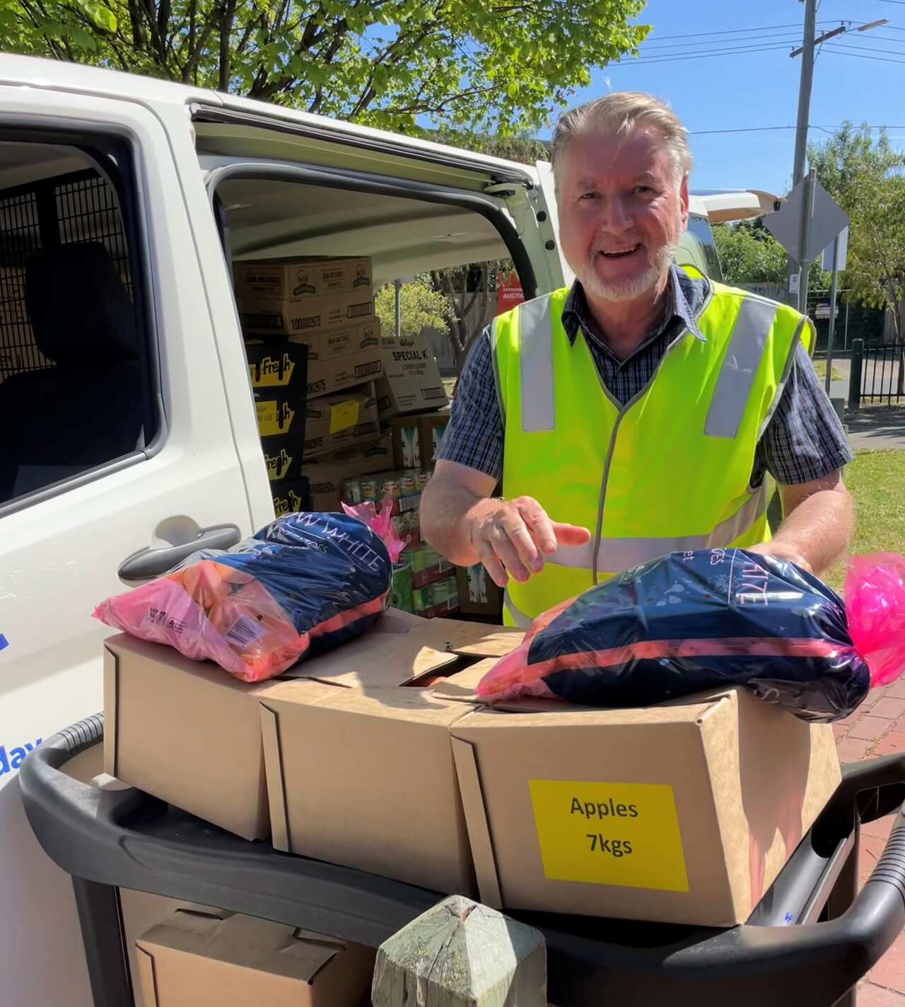 A man in a hi viz vest stands next to a trolley loaded with food.