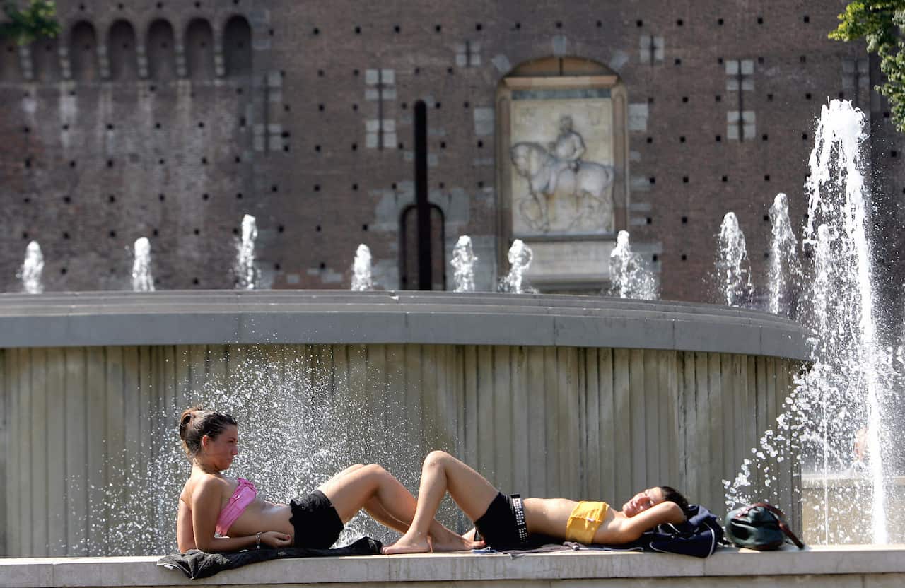 Tourists refresh and sunbathe on the side of a public fountain