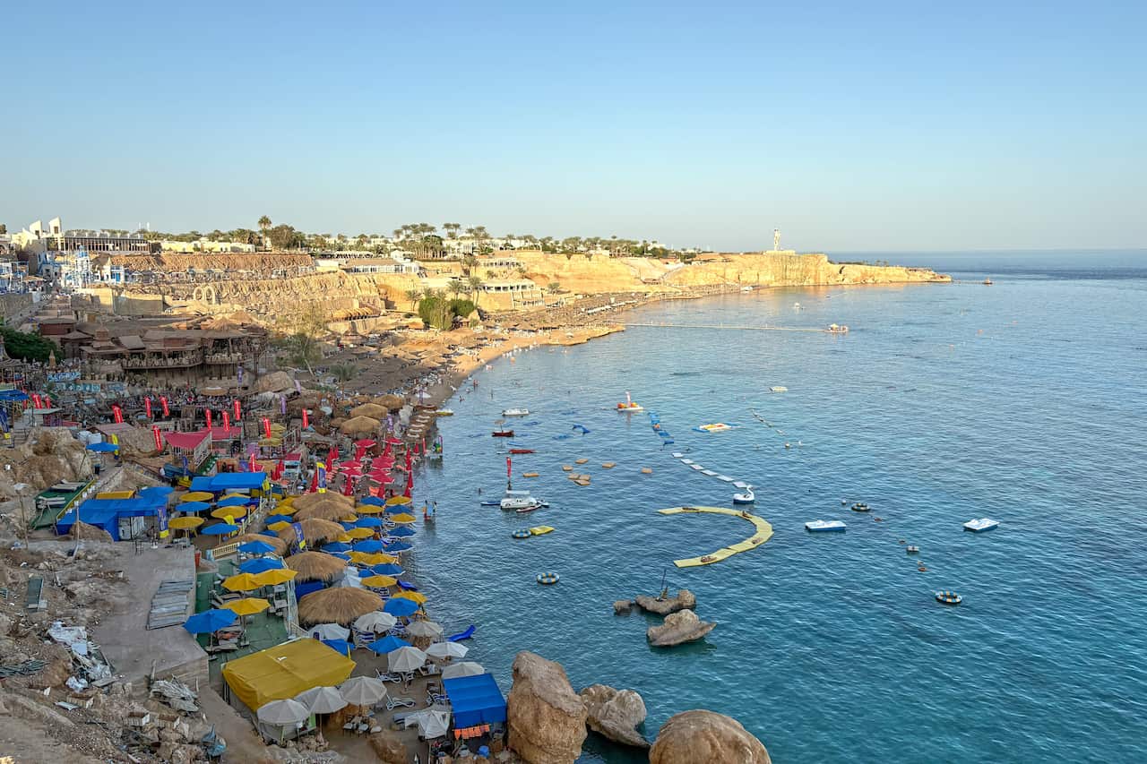 A view of a crowded beach with parasols and boats in the water.
