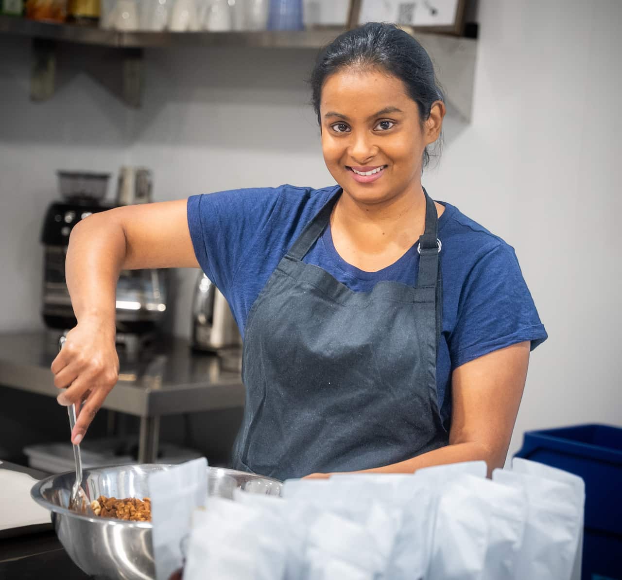A woman in a blue shirt stirs a bowl of food in a kitchen.