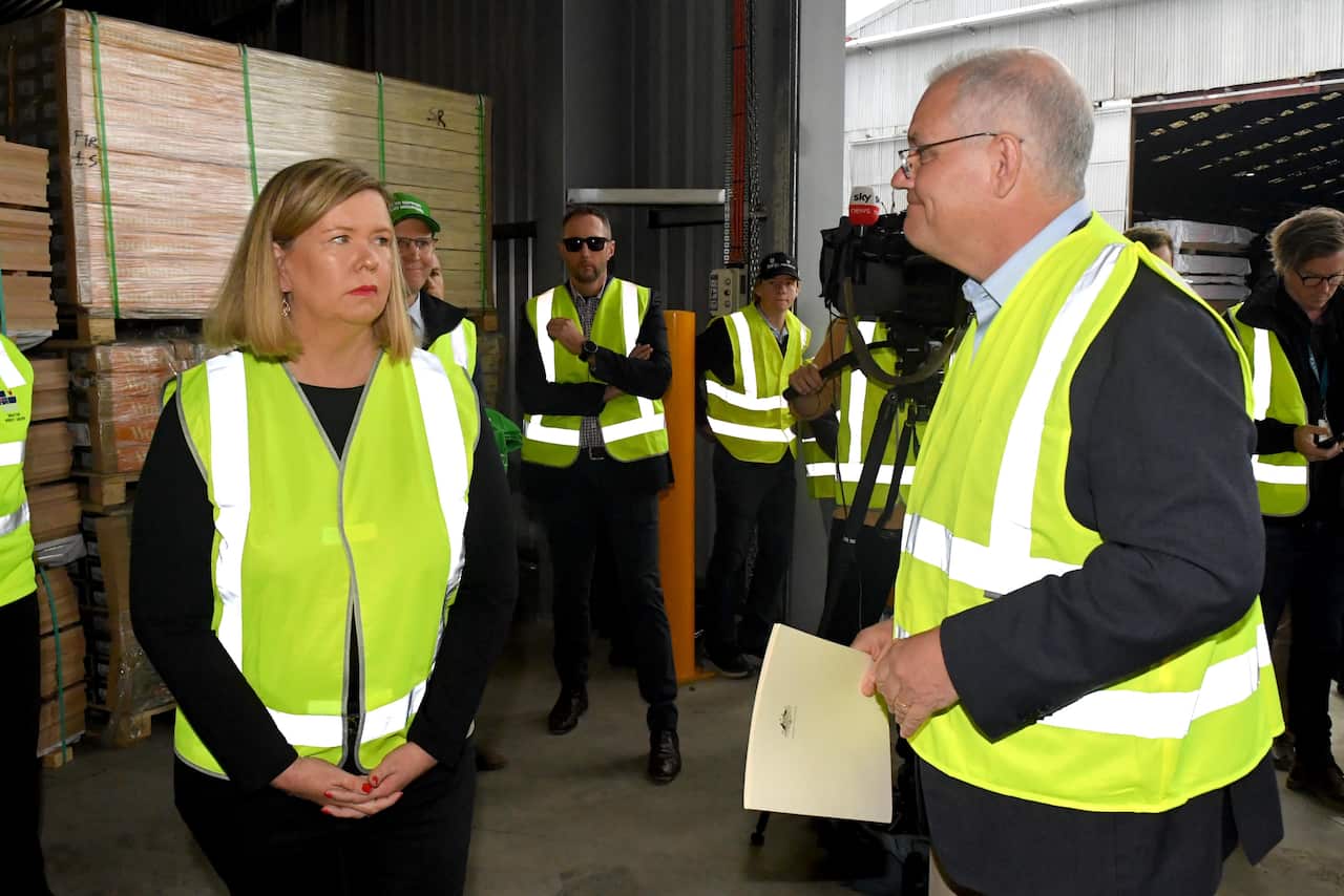 Scott Morrison smiles and a woman looks blankly. Both are wearing yellow hi-vis vests