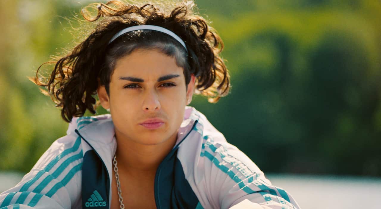 A teenage boy in a striped tracksuit top stares into the distance.