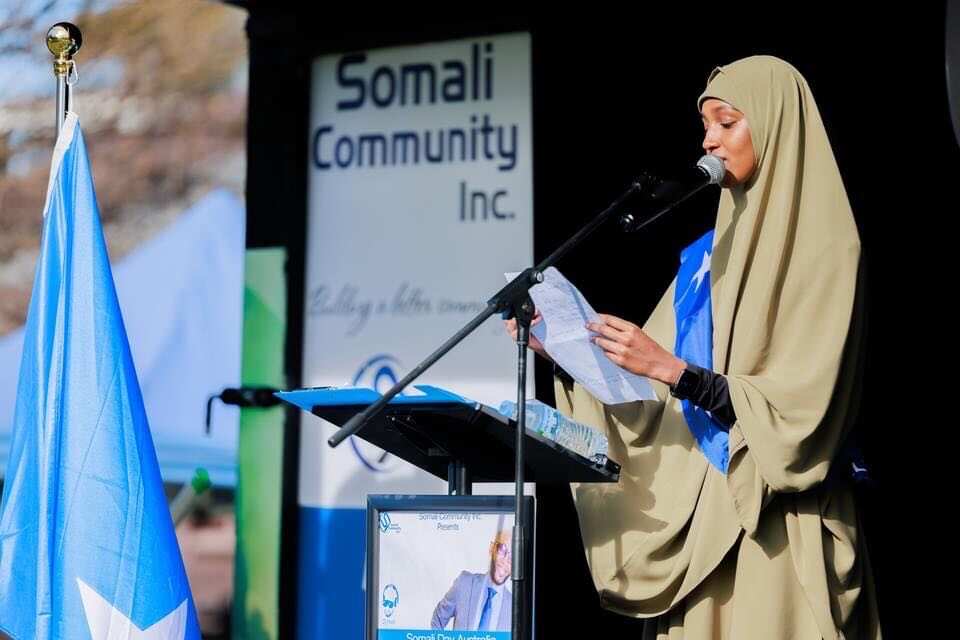 A woman stands at a podium reading from a piece of paper at a Somali community event.