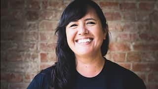 A smiling woman with long black hair and wearing a black t-shirt