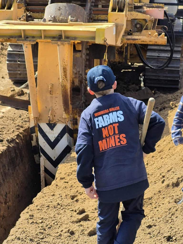 A child walking alongside a digger wearing a shirt that reads 'FARMS NOT MINES'