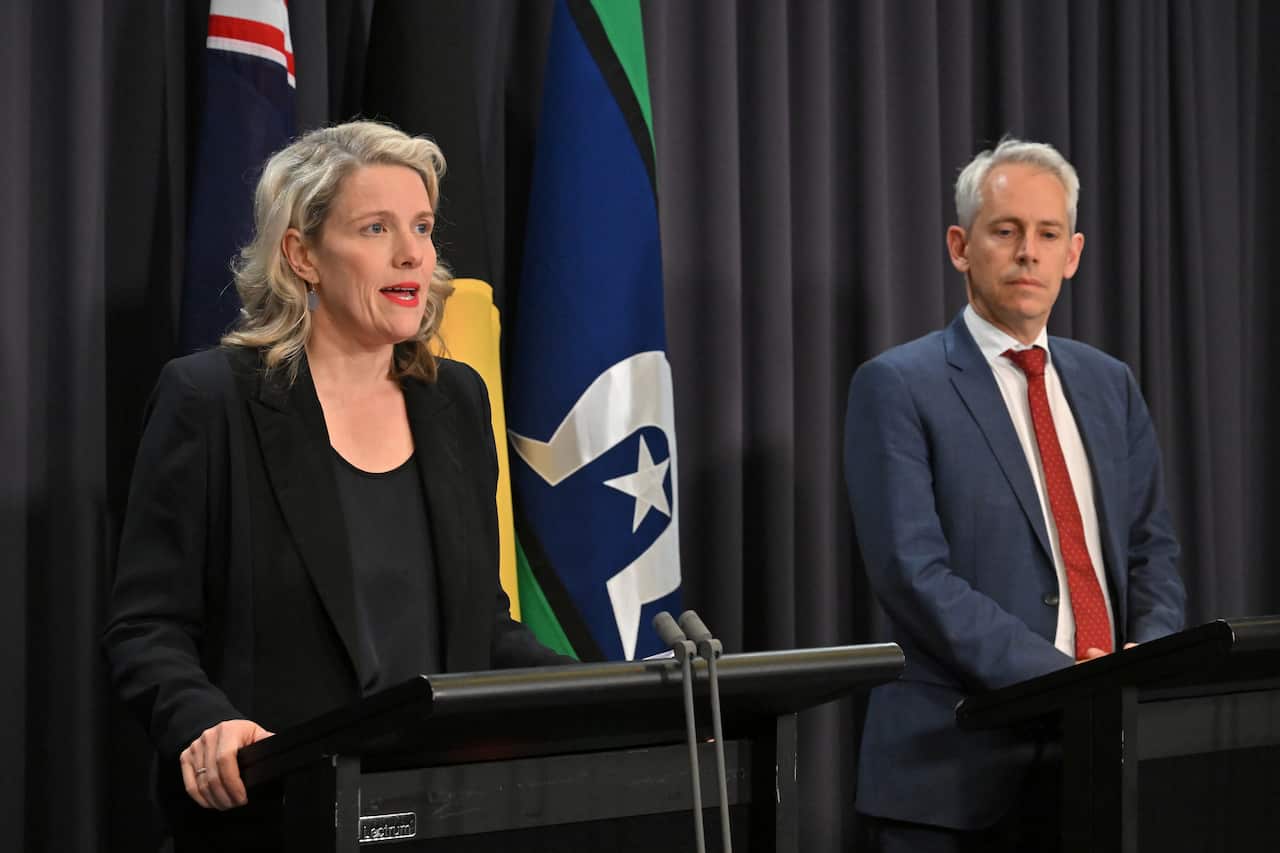 A woman speaking at a podium, with a man standing on a podium to her left
