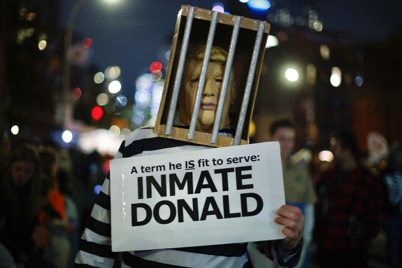 A man dressed as former US president Donald Trump behind bars, holding an "Inmate Donald" sign.