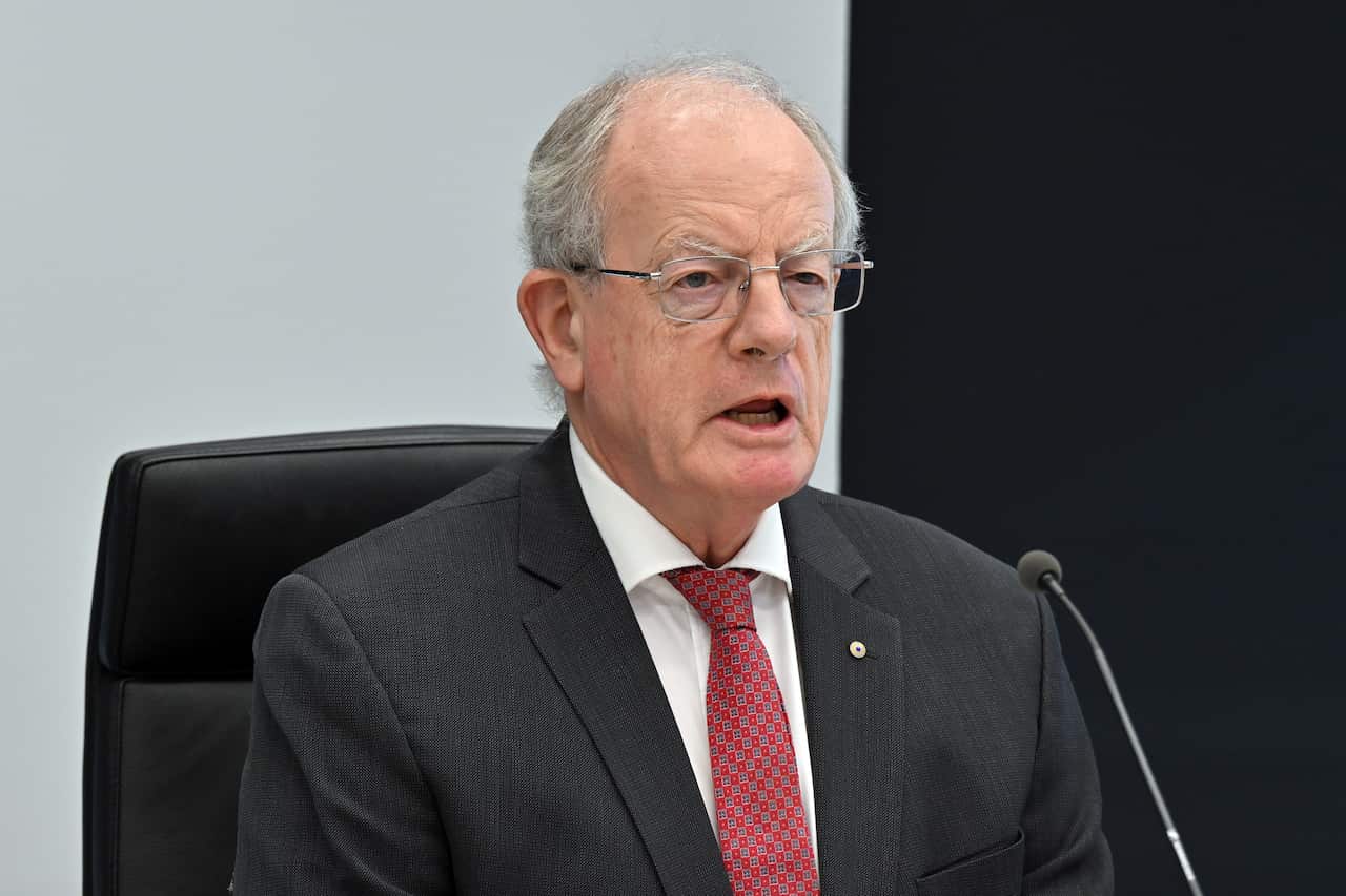 A man in a black suit and red tie speaks into a microphone.