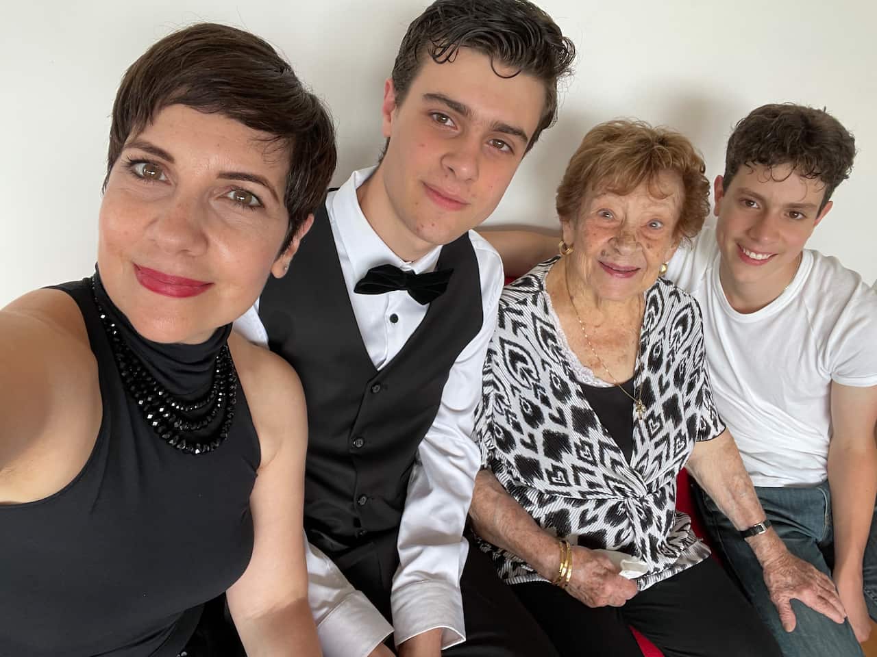 A woman takes a selfie that includes her two teenage boys and an older lady — all smiling for the camera.
