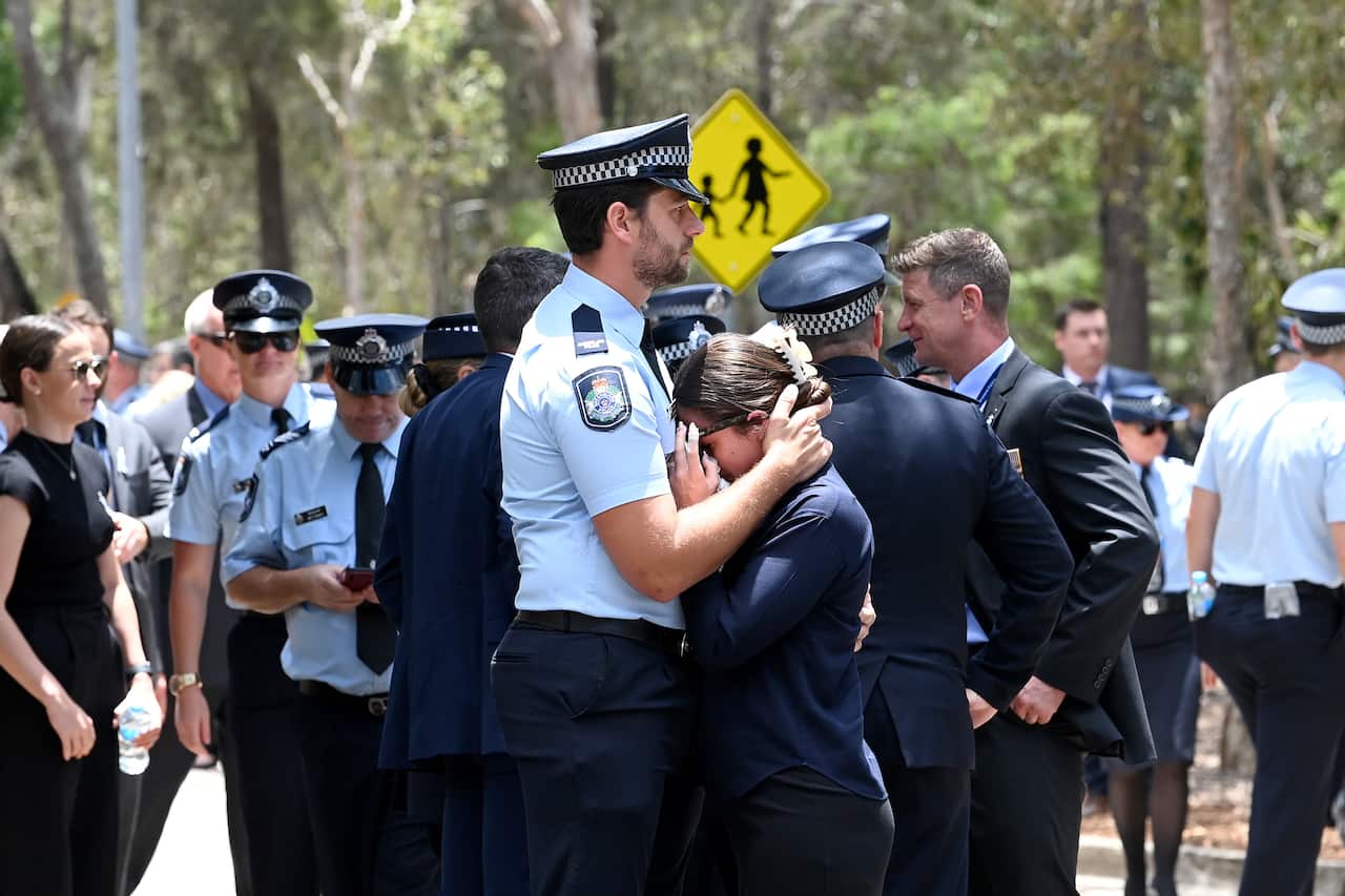 A uniformed police officer comforts a woman at the memorial service.