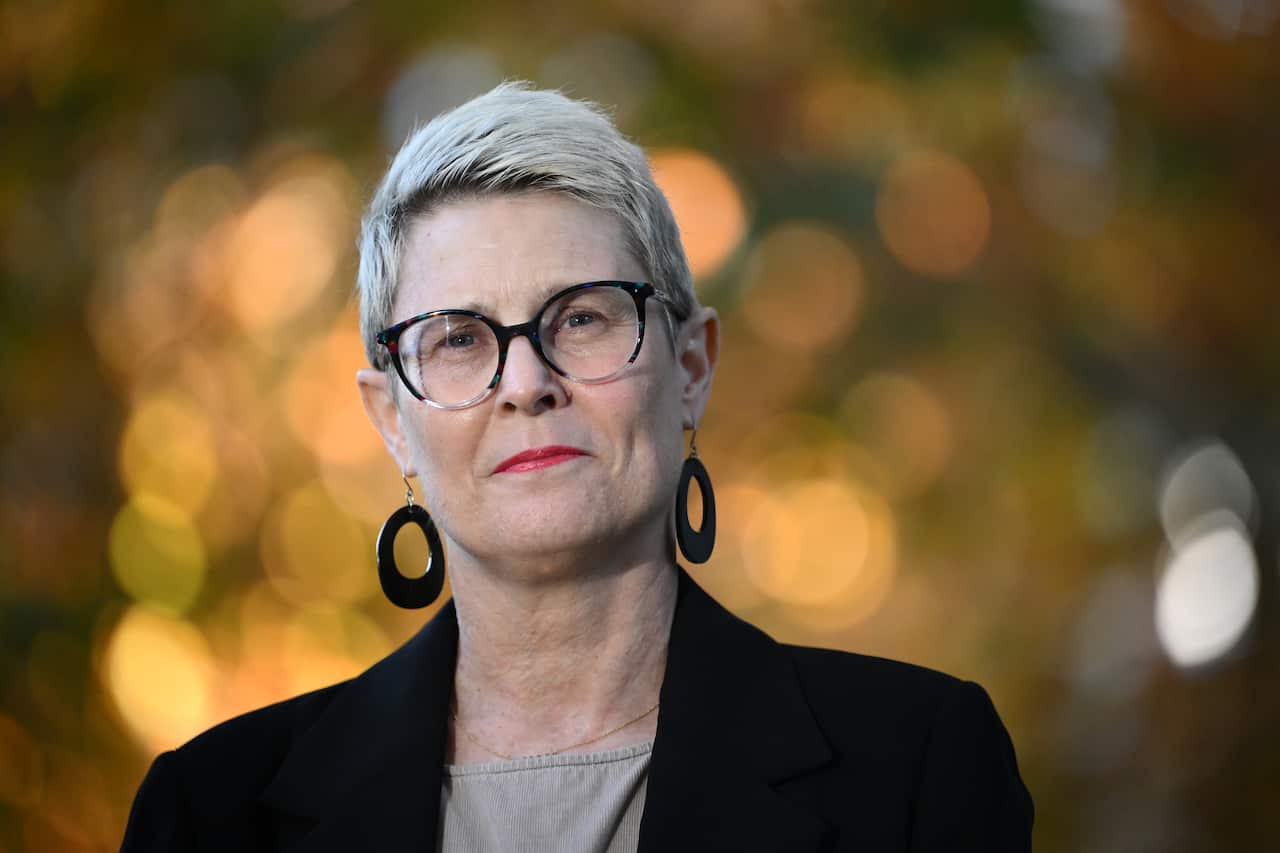 A woman wearing glasses looks at the camera