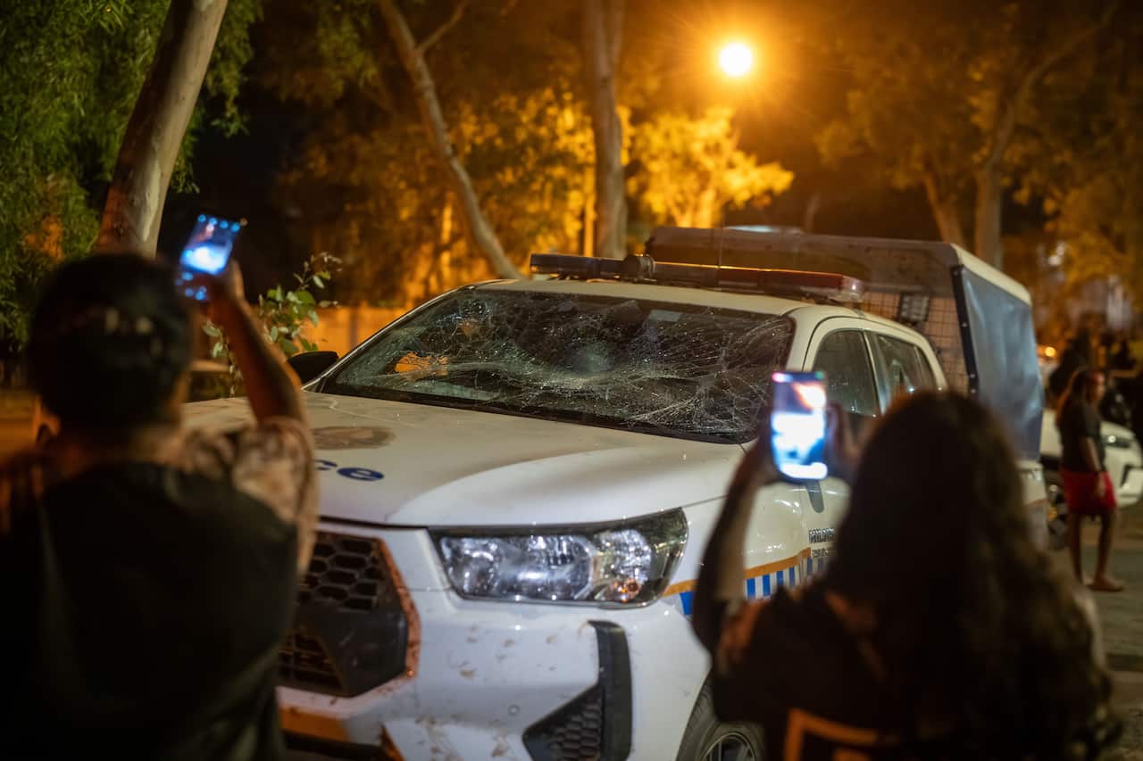 Two people hold up their smartphones to take photos of a damaged police vehicle