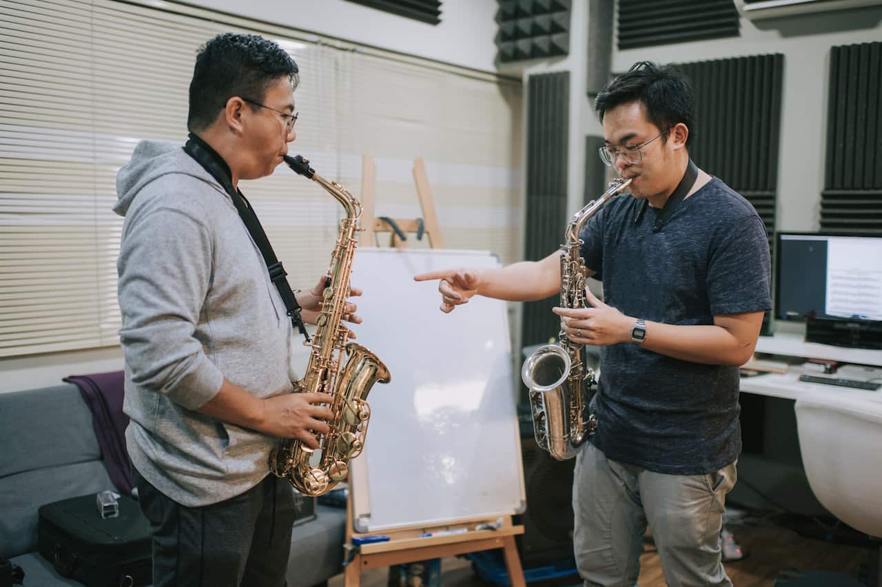 Asian chinese mid adult man learning music instrument playing saxophone from his instructor in music studio - Australia Explained – Learning an instrument