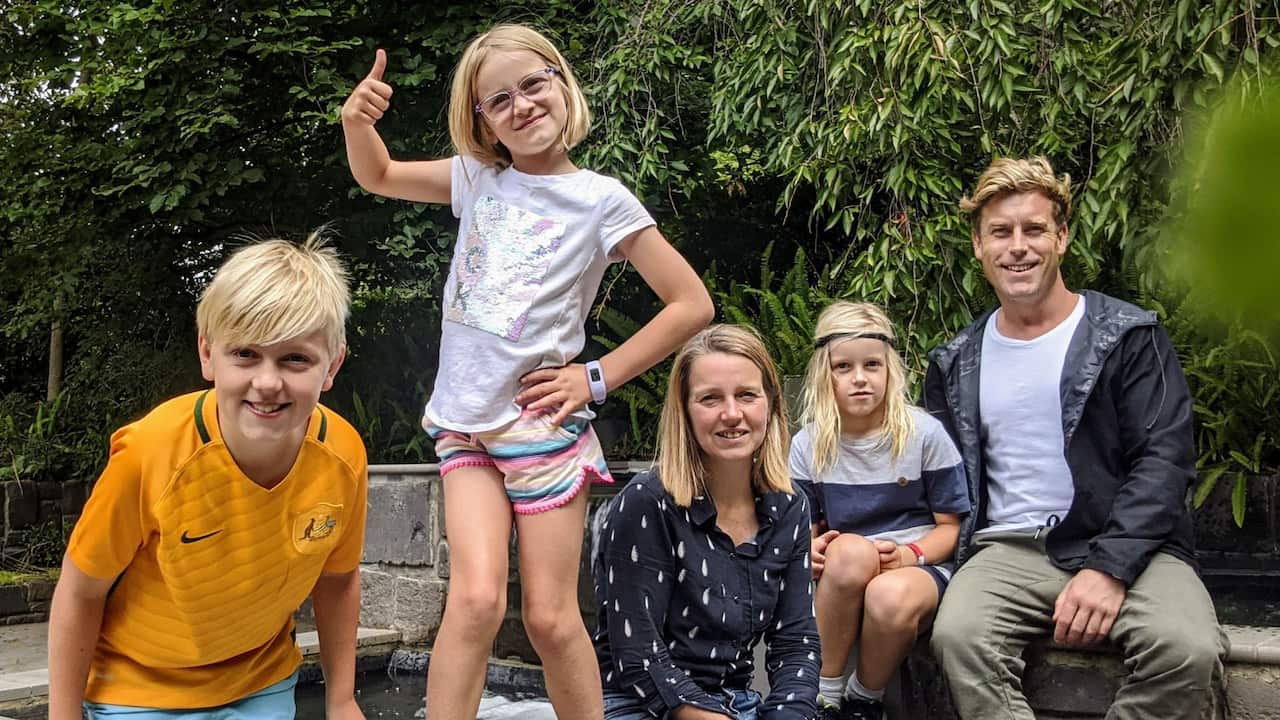 a family of three blonde children and a blonde man and blonde woman posed in a backyard