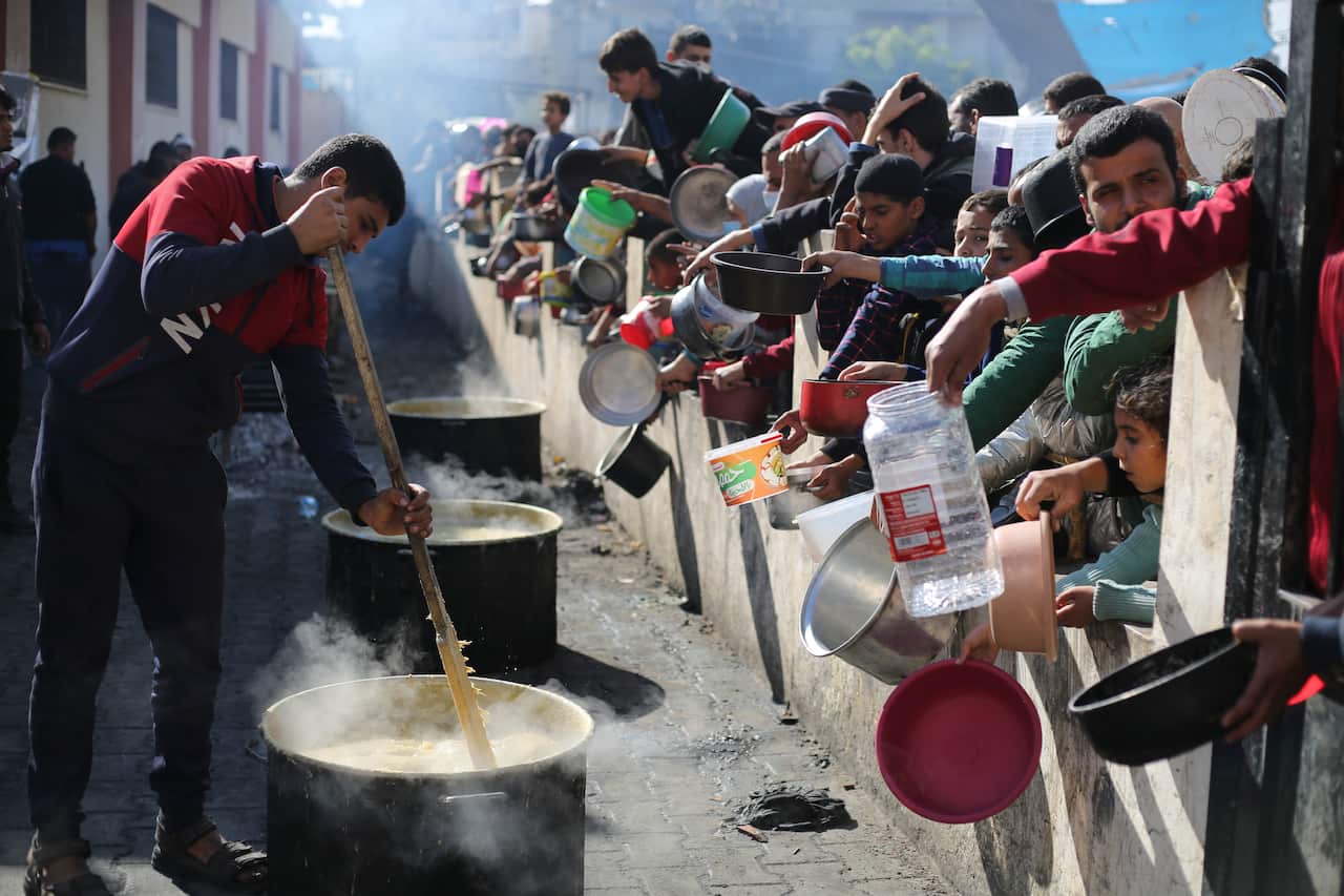 Aman stirs a large pot while others line up for food