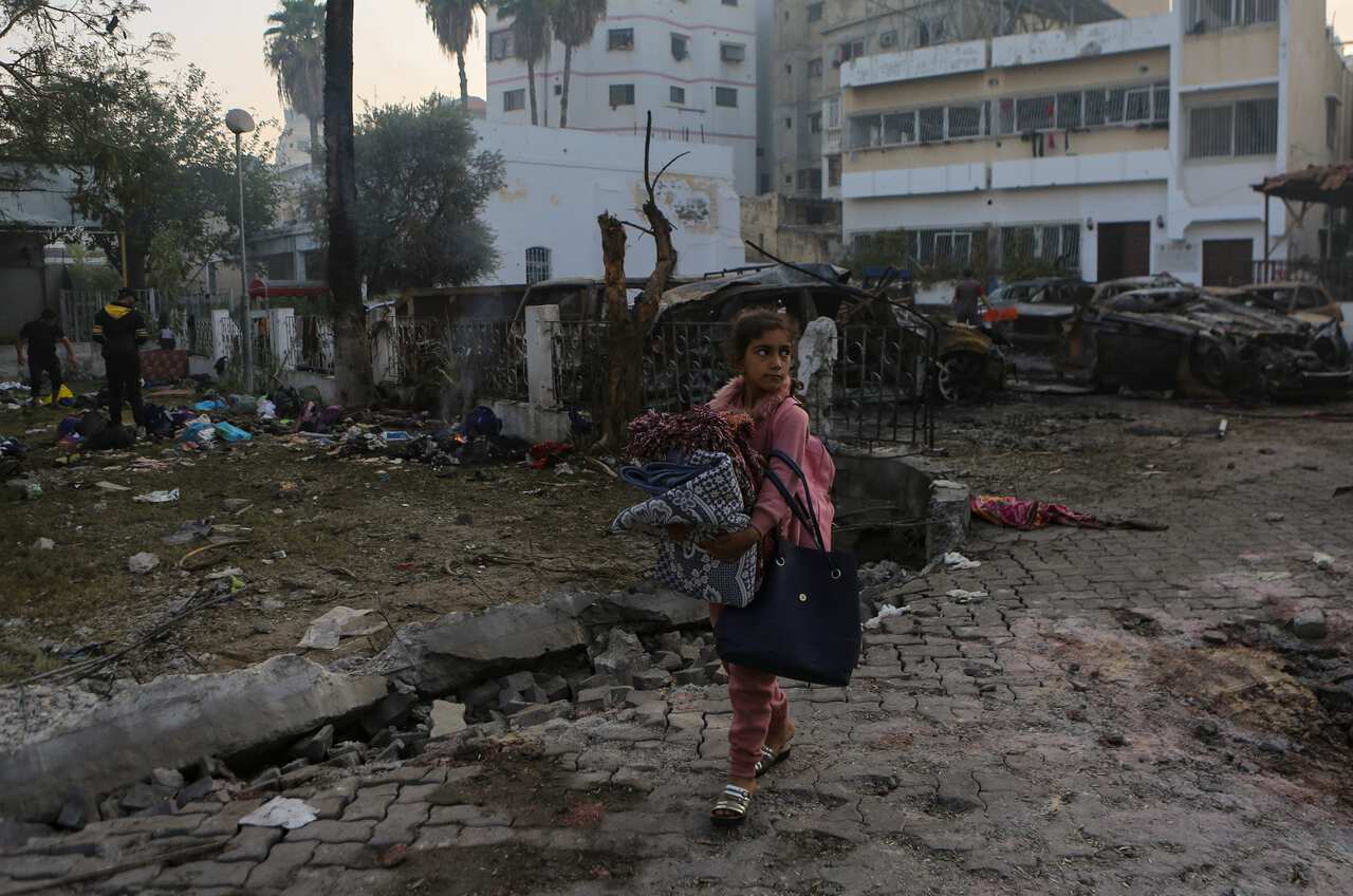 A girl walking past a site where there is debris and burnt-out cars.