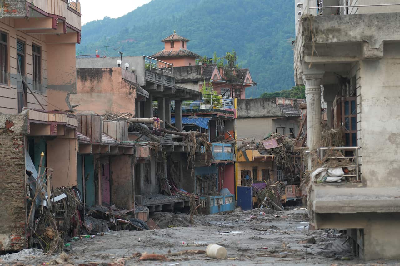 Flood-damaged street in Nepal, with mud and debris covering the road and several buildings heavily damaged by floodwaters.