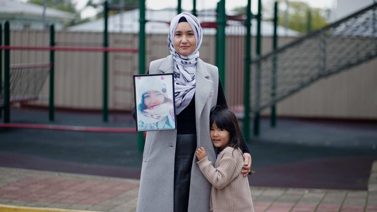 A woman holds a framed photograph. Her young daughter is at her side.