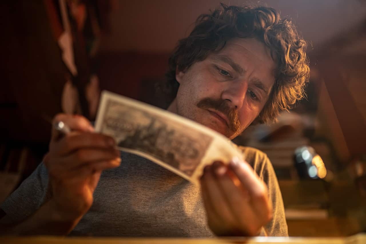 A man sits studying a piece of paper while holding a cigarette