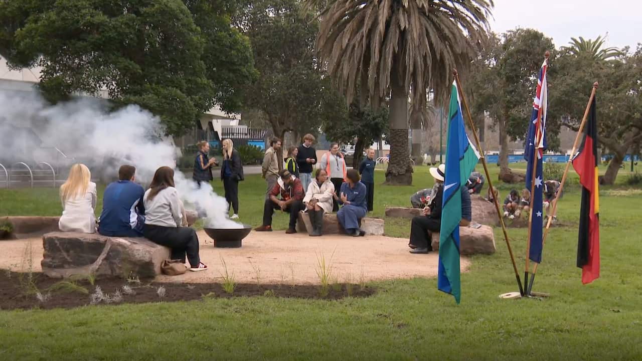 People sitting on large rocks placed in a circle around an open fire.