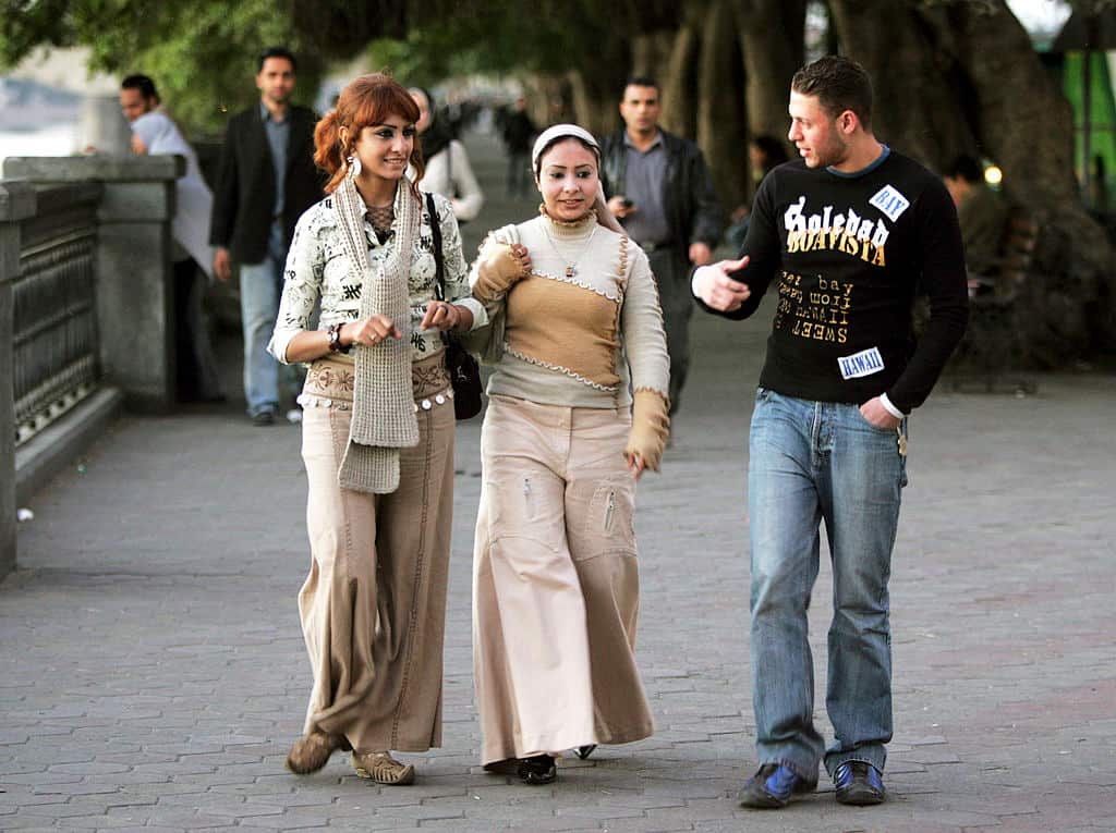 Two teenage girls and a teenage boy walk down the road together as they smile and talk.