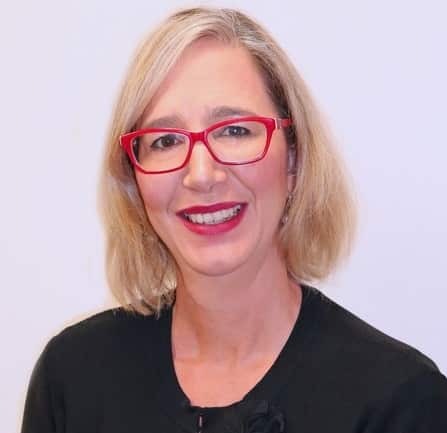  A blonde woman wearing a black top and red glasses smiles for the camera 
