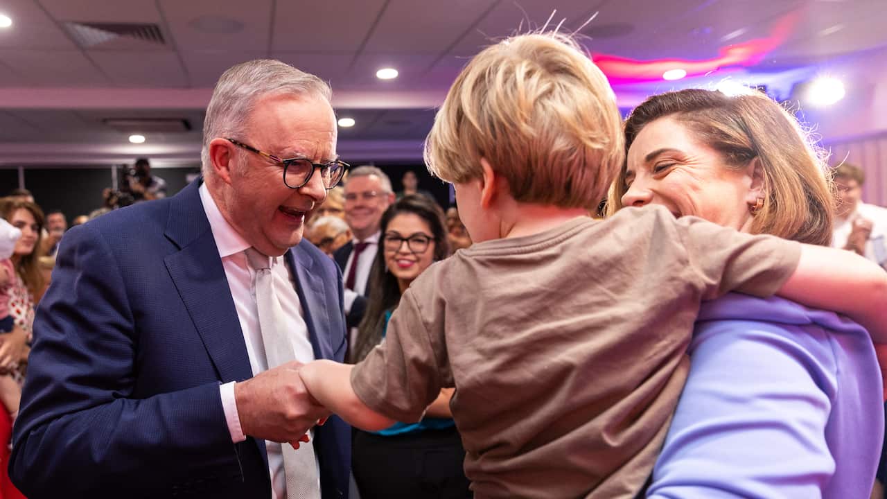 Anthony Albanese shaking the hand of a young child, who is being held by his mother.