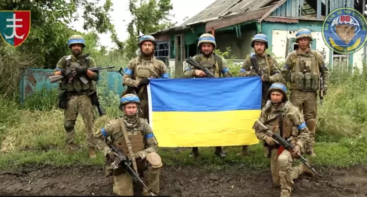 Ukrainian soldiers with Ukrainian flag in front of a house in recaptured area