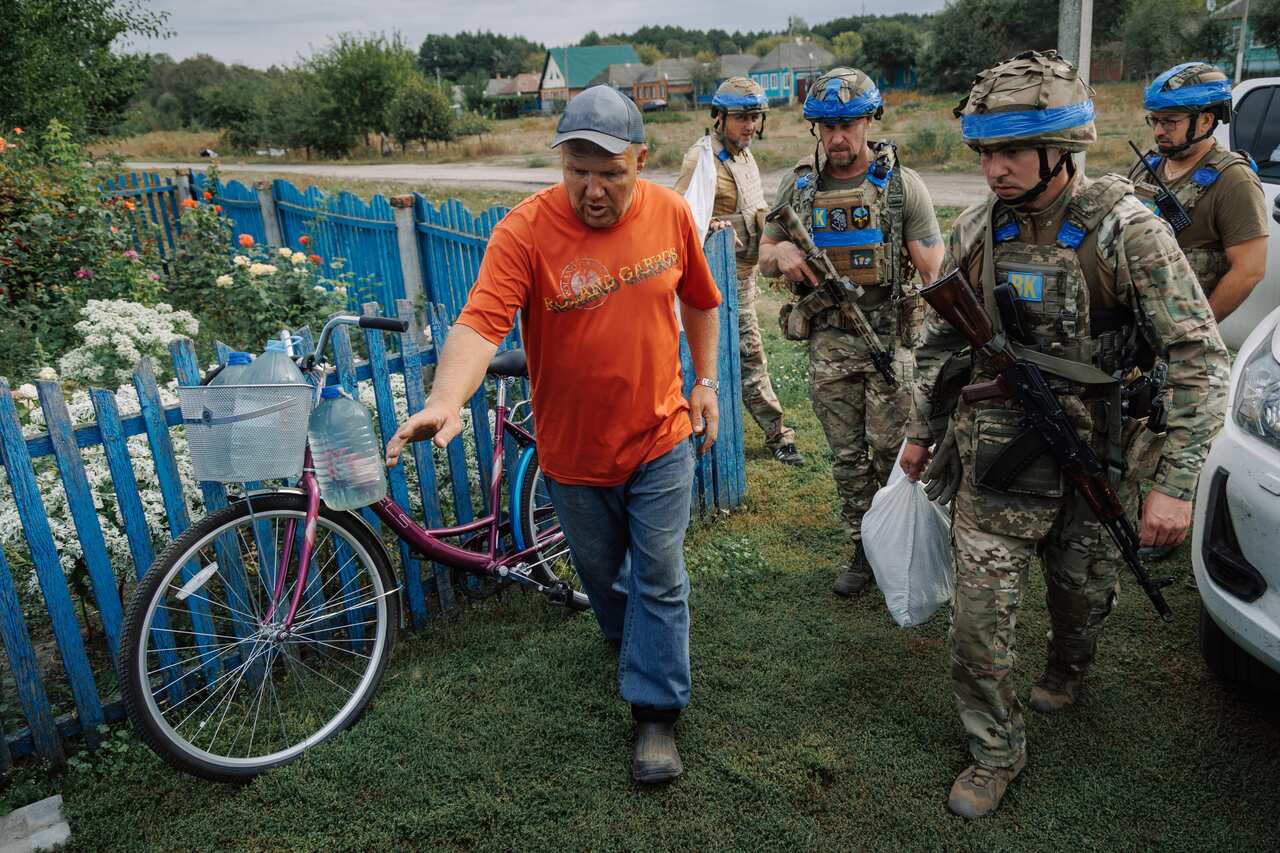Soldiers speaking to a man outside a house.